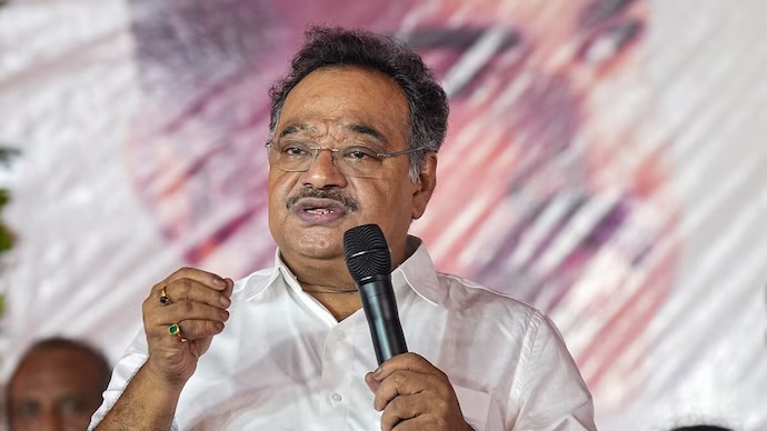 Samik Bhattacharya speaking at a public event, holding a microphone and gesturing with his left hand