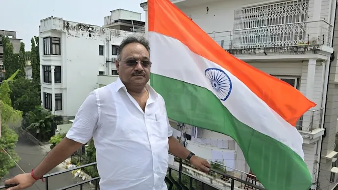 Samik Bhattacharya standing on a balcony beside a large Indian national flag in a residential neighbourhood