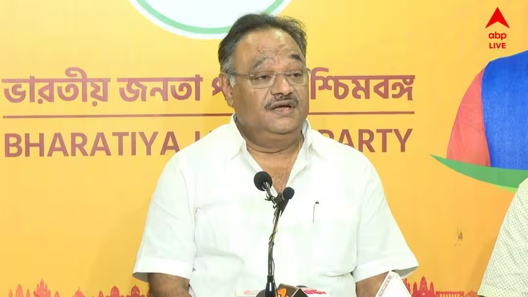 Samik Bhattacharya speaking at a media briefing in front of a yellow Bharatiya Janata Party backdrop with Bengali lettering