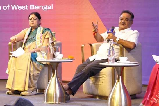 Samik Bhattacharya seated on a panel stage, gesturing while holding a microphone, with another panellist beside him