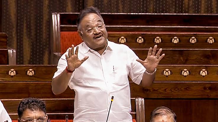 Samik Bhattacharya standing to speak in the Rajya Sabha chamber with both hands raised, members seated behind him
